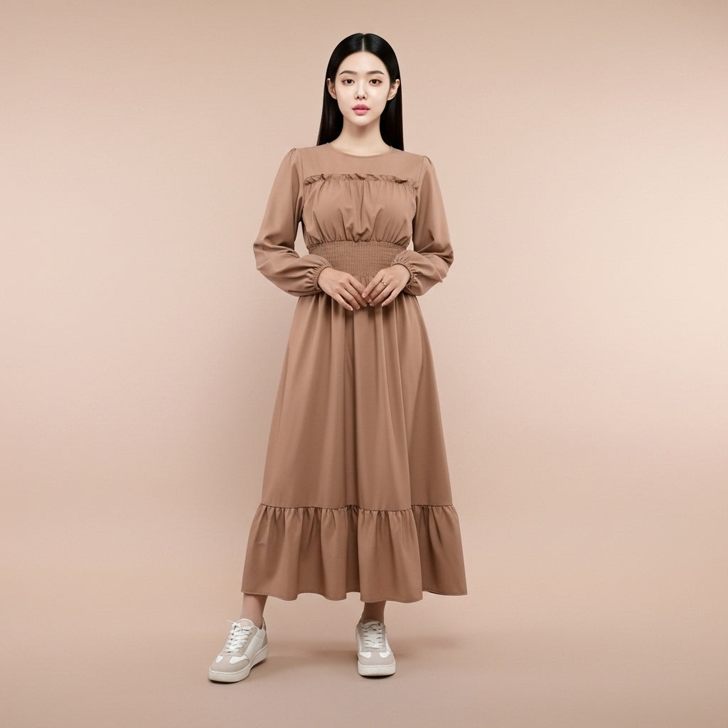 Shirred waist maxi dress in khaki worn by a standing model facing front, showing a round neckline, long gathered sleeves with elastic cuffs, shirred elastic waistband, softly pleated bodice, flowing full-length skirt, and lotus-style hem finishing at ankle length