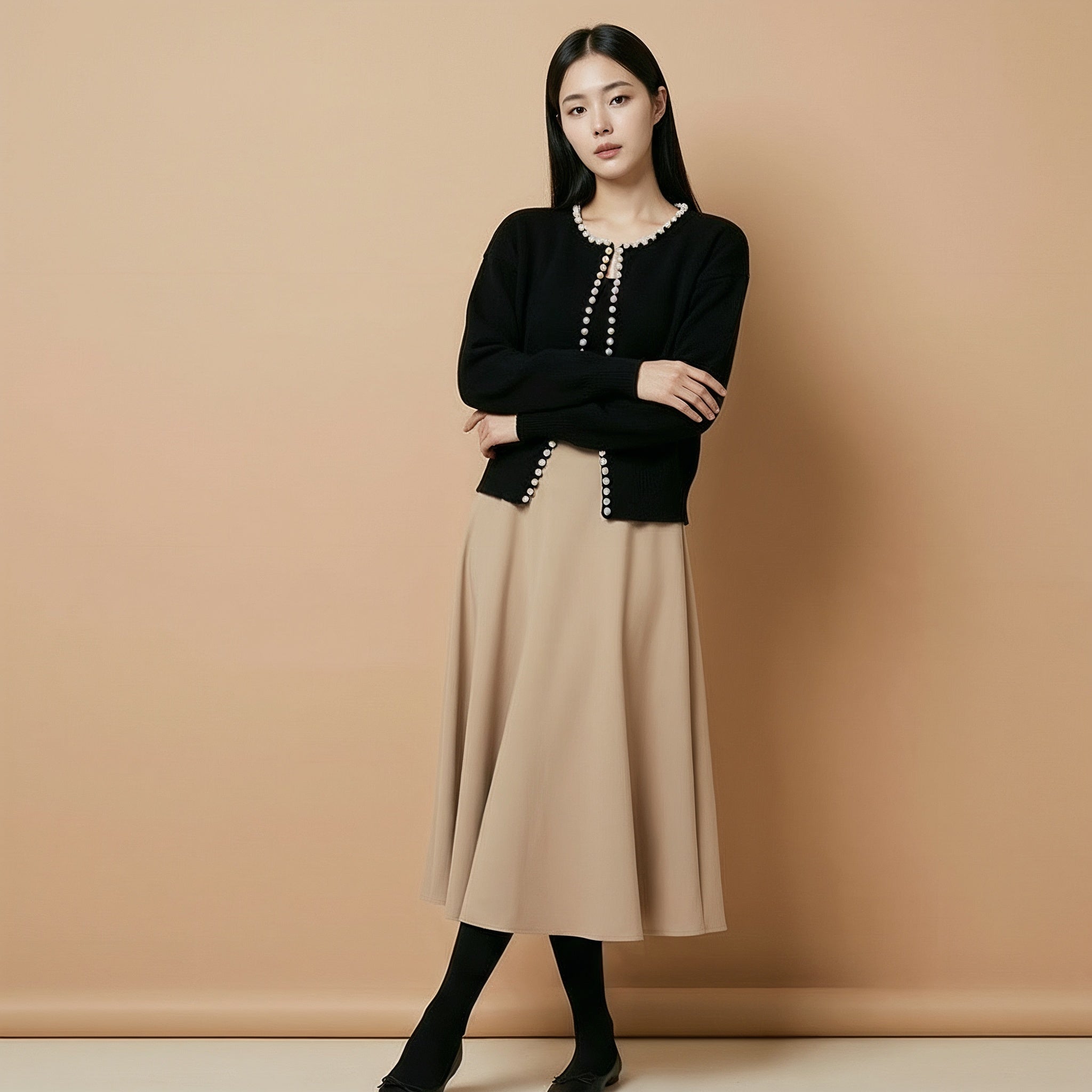 Cropped v neck cardigan in black worn by a standing model, showing a cropped length, long sleeves, pearl button trim, and open-front design