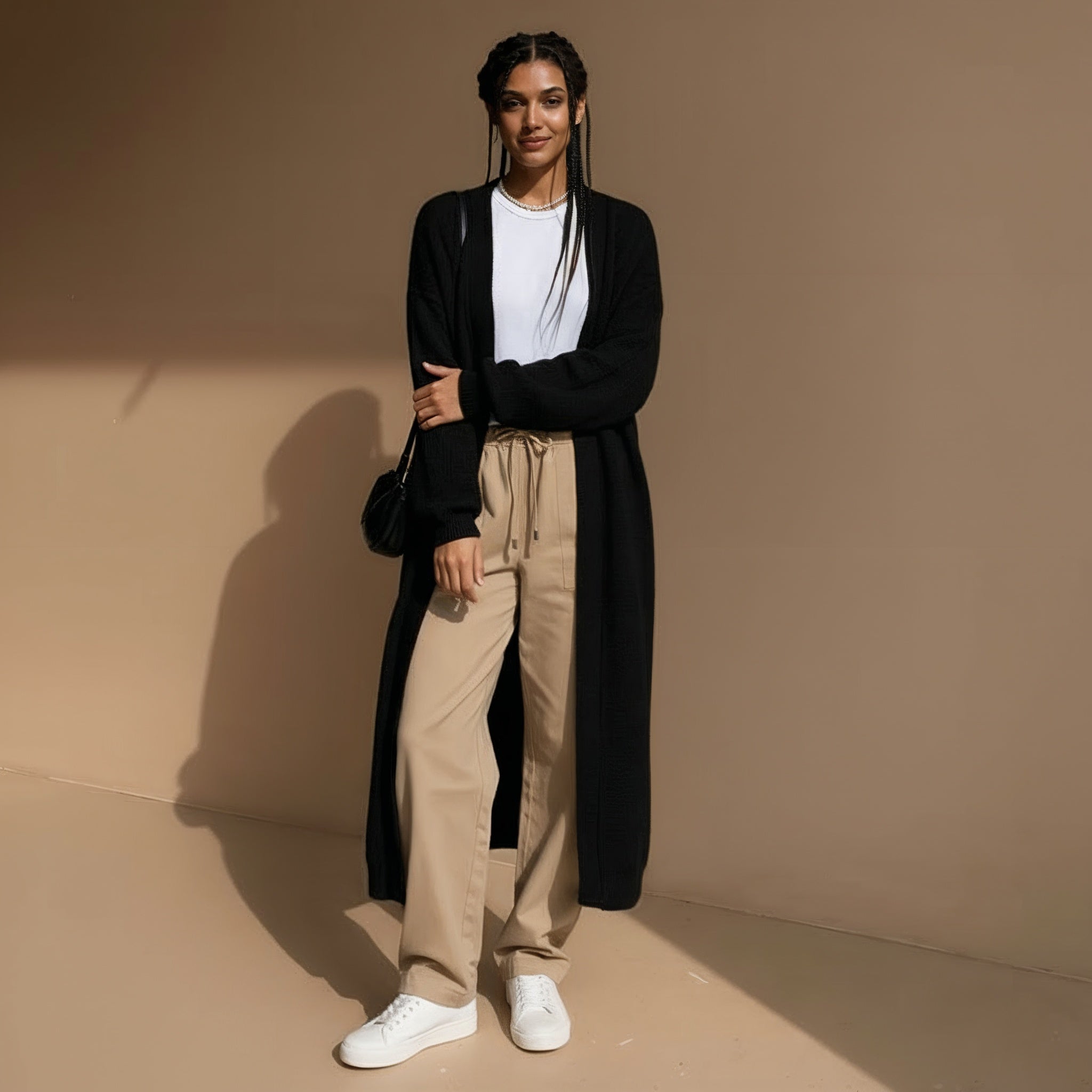 Longline knit cardigan in black worn by a standing model, showing an open front, oversized fit, long straight silhouette, and relaxed sleeves