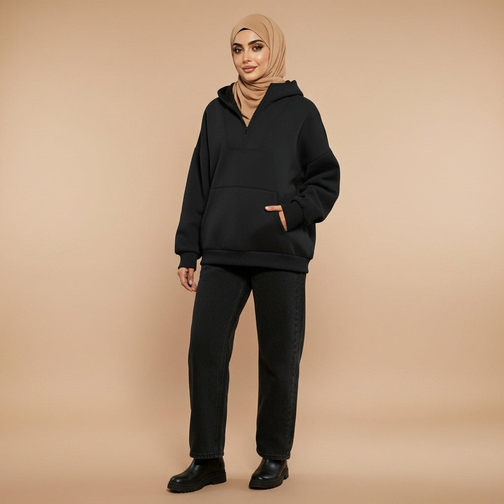 Quarter zip sweatshirt in black worn by a standing model, showing a loose fit, quarter-length zip neckline, long sleeves, ribbed cuffs, and kangaroo pocket
