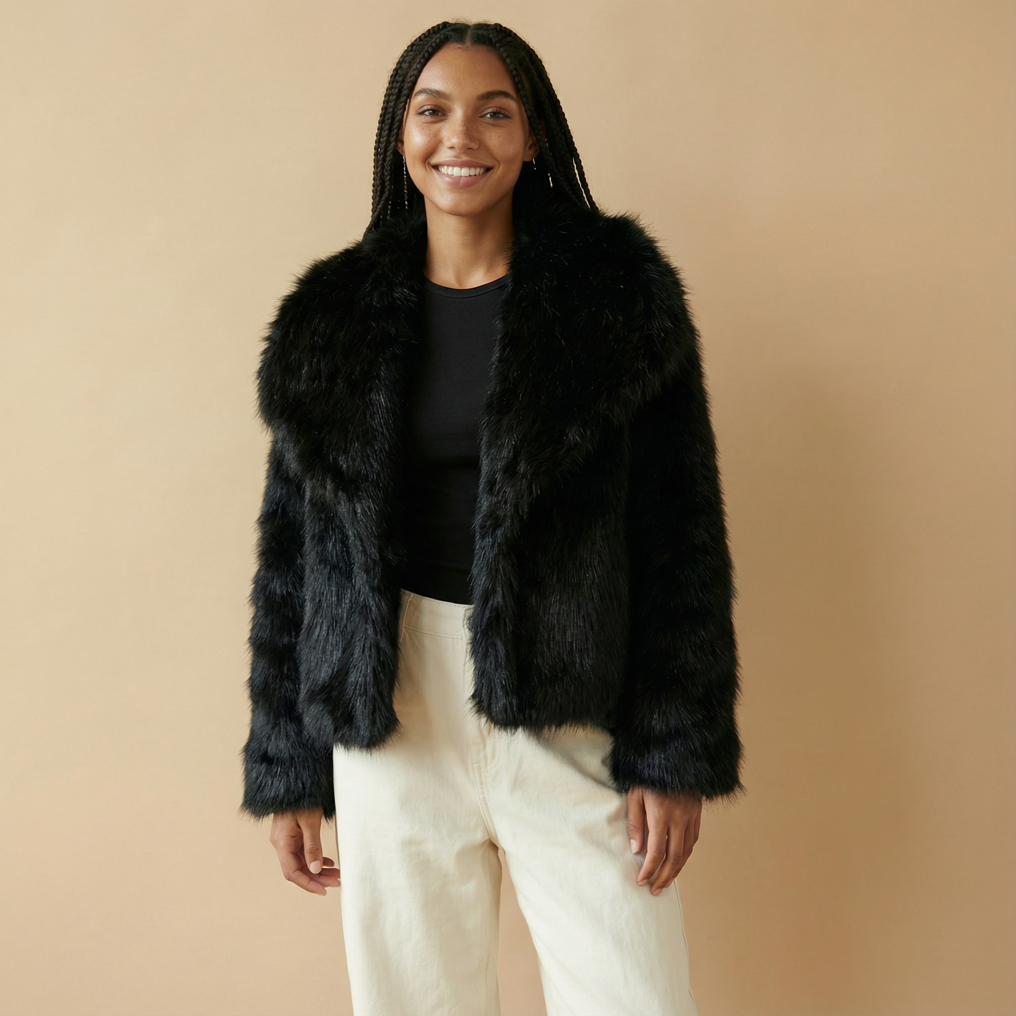 Cropped faux fur jacket in black worn by a standing model, showing a short cropped silhouette, full plush faux fur texture, wide collar, long sleeves, and open front construction