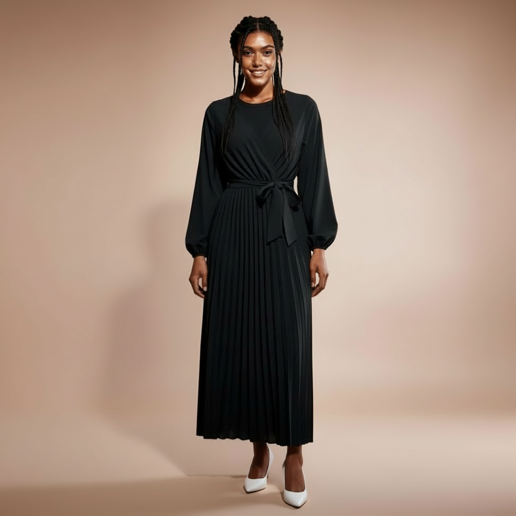 Pleated V-neck maxi dress in black worn by a standing model facing front, showing a wrap-style V neckline, long sleeves with gathered cuffs, self-tie waist belt, finely pleated skirt, and mid-calf to ankle-length hem