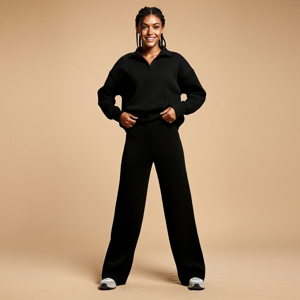 Wide leg tracksuit set in black worn by a standing model facing front, showing an oversized sweatshirt with open collar neckline, dropped shoulder seams, long sleeves, matching wide leg joggers with straight loose fit, full-length legs, and clean monochrome silhouette