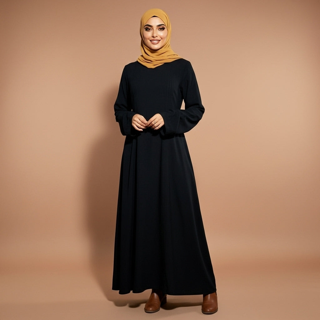 Long sleeve winter maxi dress in black worn by a standing hijabi model facing front, showing a round neckline, full-length sleeves, clean front panel, flowing A-line shape, full-length skirt, and structured fabric fall to the ankles