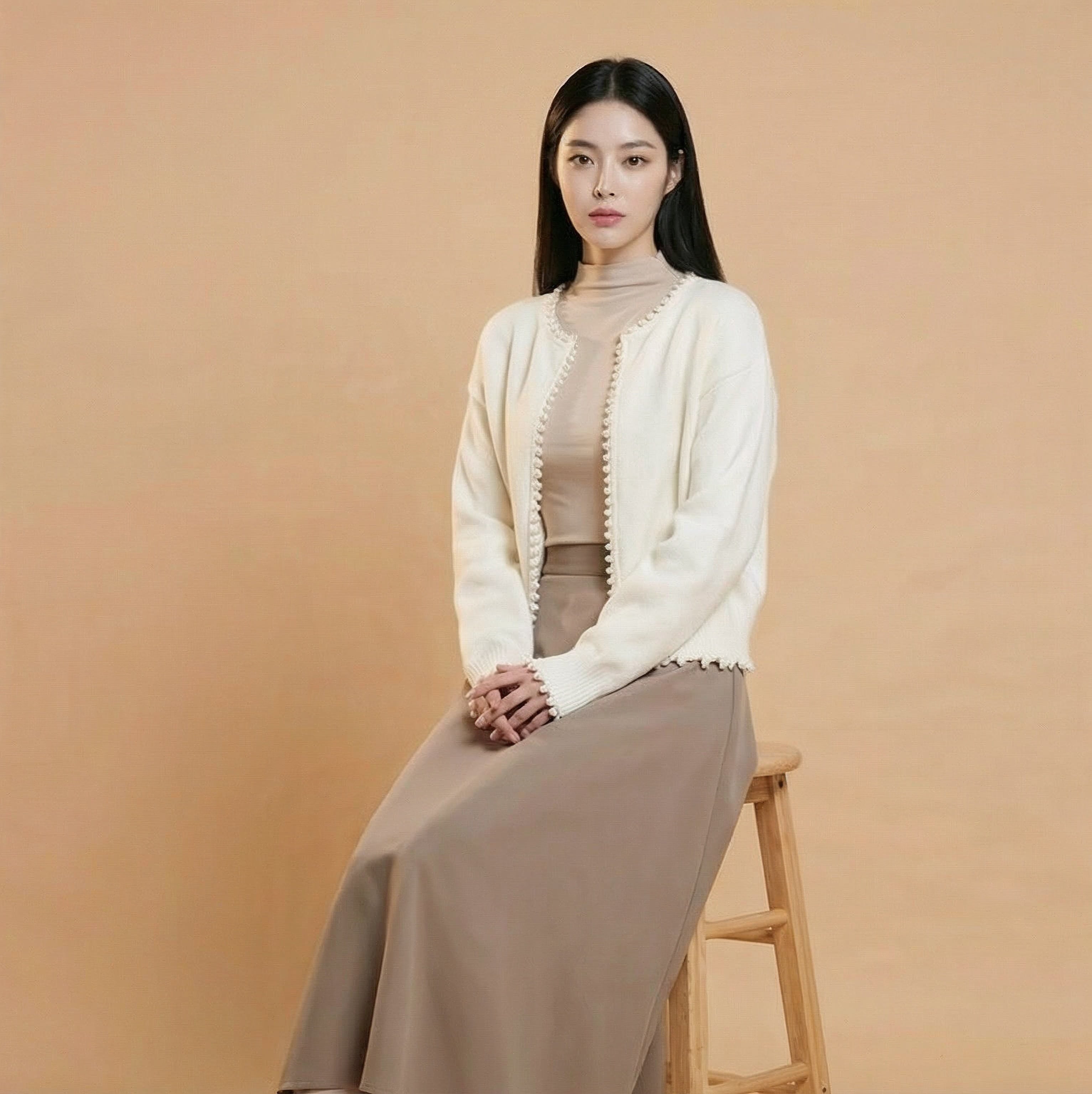 Cropped v neck cardigan in white worn by a seated model, showing a cropped hem, long sleeves, pearl button trim, and relaxed drape
