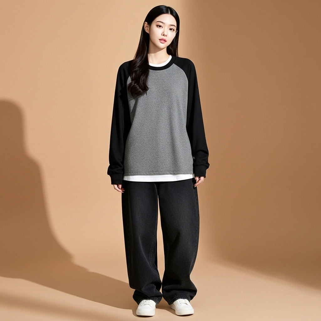 Oversized long sleeve raglan top in Grey and black worn by a standing model facing front, showing contrast raglan sleeves, crew neckline, relaxed straight hem, loose fit silhouette, and full-length sleeves